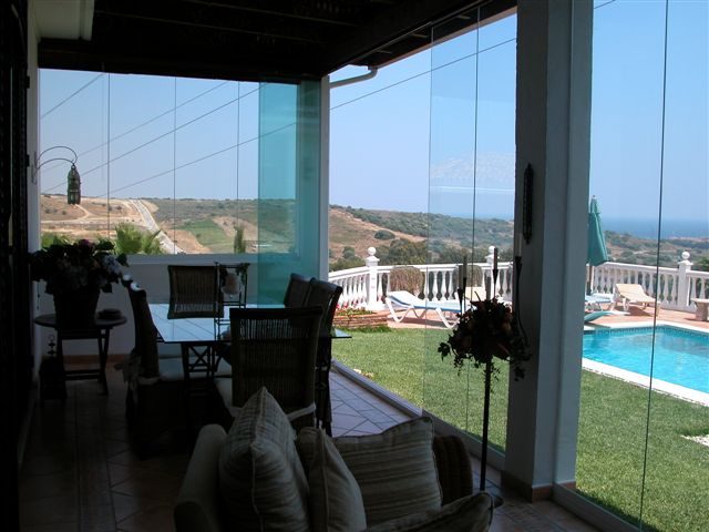 Terraza con vista al mar y cortinas de cristal semiabiertas